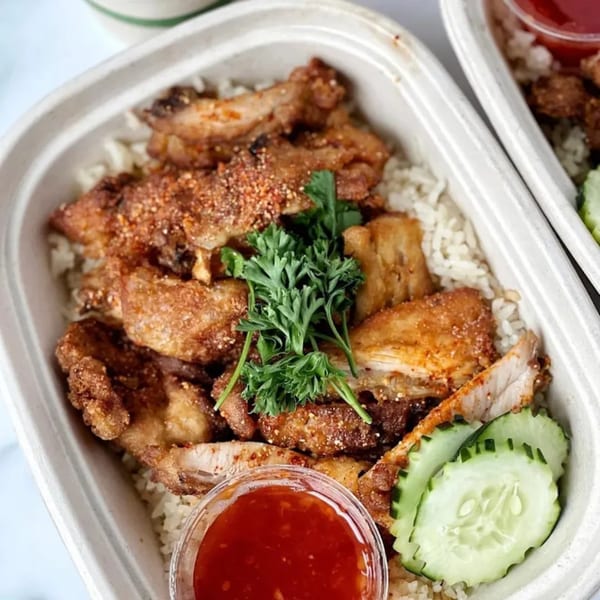 Crispy fried chicken over rice with fresh parsley, cucumber slices, and chili sauce.