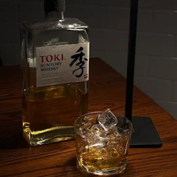 A bottle of Suntory Toki Whisky next to a glass of whisky with ice on a wooden table.