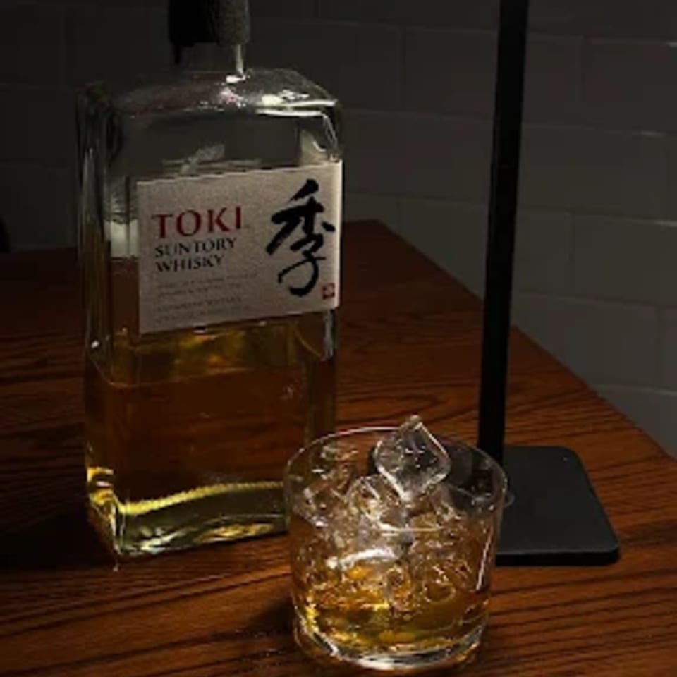 A bottle of Suntory Toki Whisky next to a glass of whisky with ice on a wooden table.