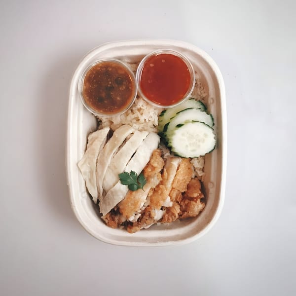 Hen's Thai chicken and rice dish with two sauces and cucumber slices in a takeout container.