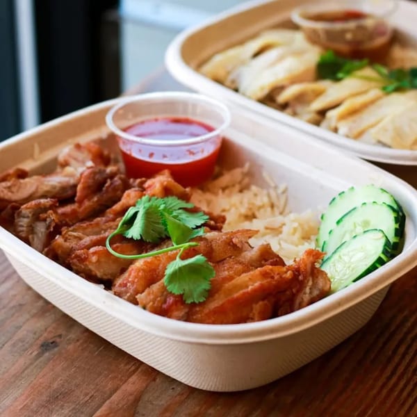 Two takeout containers of Hen's Thai fried chicken and rice, with cucumber and sauce.