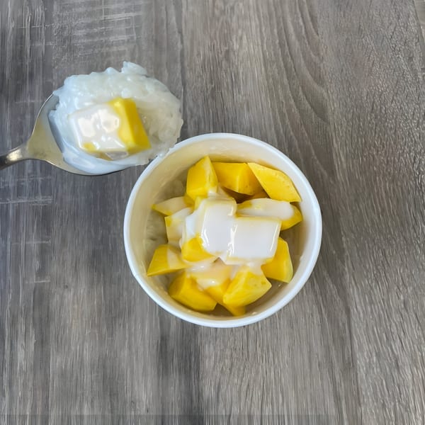 A spoon of sticky rice and mango next to a cup of mango and coconut cream.