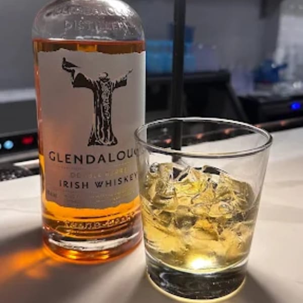 A bottle of Glendalough Irish Whiskey next to a glass of whiskey with ice on a bar.