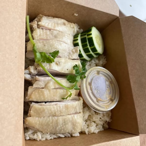 Thai chicken and rice with sliced cucumbers and a sauce cup in a takeout box.