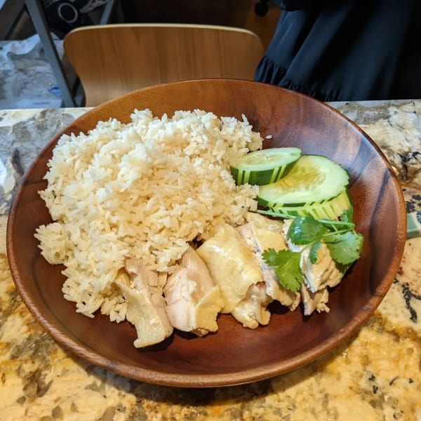 A wooden bowl of Hen's Thai chicken and rice, garnished with cucumber and cilantro.