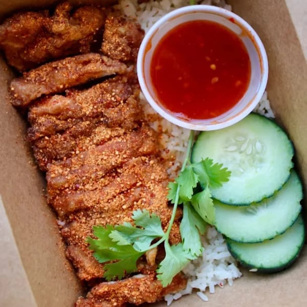 Crispy Thai fried chicken with rice, sweet chili sauce, cucumber slices, and cilantro in a takeout box.