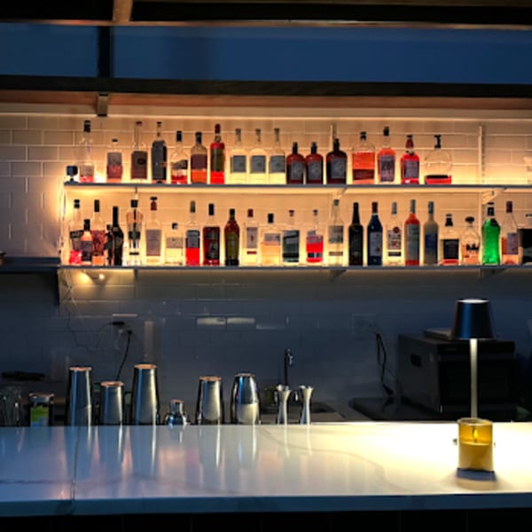 A well-stocked bar at Hen restaurant with various liquor bottles on illuminated shelves above a white counter.
